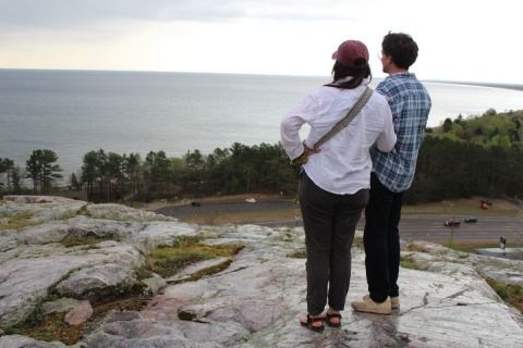 Two people stand at the top of a rock cliff overlooking Lake Superior