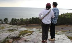 Two people stand at the top of a rock cliff overlooking Lake Superior